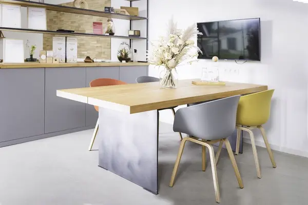 Moderner Besprechungsraum mit Holztisch, bunten Stühlen und dekorativem Trockenblumenstrauß.