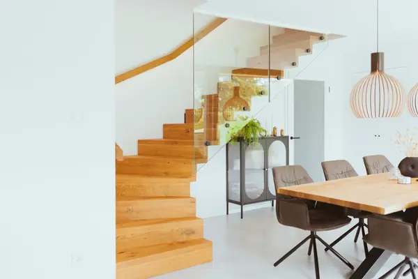 Moderne Holztreppe mit Glasgeländer in hellem Esszimmer mit Designmöbeln und Pflanzen.