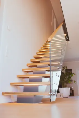 Moderne Holztreppe mit Glasgeländer und LED-Beleuchtung in einem hellen Wohnzimmer.